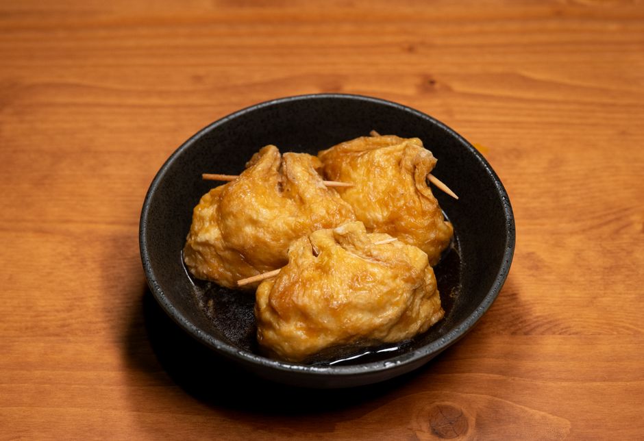 Three savory inari sushi rolls served in a dark bowl on wooden table.