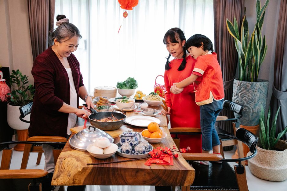 Cheerful ethnic grandmother preparing meal in frying pan for celebrating Chinese holiday with grandchildren at home
